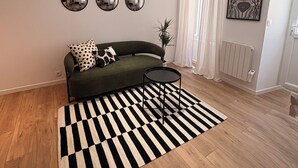 A modern living room with a sofa, a round coffee table, a black and white rug, three wall mirrors, and a radiator.