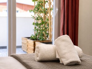 A neatly made bed with folded towels and a view of a balcony with a plant and wooden planter. - Dama Residence (Tirana)