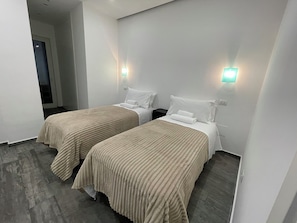 A hotel room with two beds, each with a beige bedspread, white pillows, and a nightstand. There are wall-mounted lights on either side of the beds. - Elegant 2-Bedroom, 2-Bathroom Apartment | AC | Metro Line C (Roma)