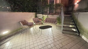 Eine Terrasse im Freien mit gefliestem Boden, zwei gepolsterten Stühlen, einem kleinen Tisch und einer Treppe.
