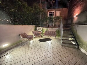 An outdoor patio with tiled flooring, two cushioned chairs, a small table, and a staircase. - Elegant 2-Bedroom, 2-Bathroom Apartment | AC | Metro Line C (Roma)