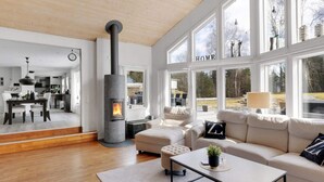 A modern living room with a stone fireplace, large windows, a sofa, and a coffee table. - 5 Star Holiday Home in Svanesund (Svanesund)