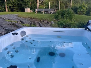 A hot tub with multiple jets, surrounded by a natural setting with a bench and trees. - 5 Star Holiday Home in Svanesund (Svanesund)