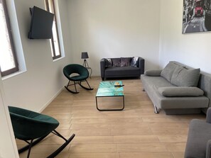 A living room with a sofa, a rocking chair, a coffee table, and a TV mounted on the wall. - Vrbo Property (Anceaumeville)