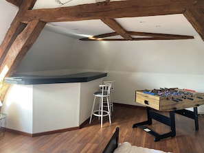 A loft-style room with exposed wooden beams, a bar area, a foosball table, and a seating area with stools. - Vacation rental 10 minutes from Rouen: pool, sauna, spa, pétanque court, foosball table (Anceaumeville)