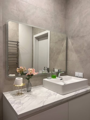 Un baño moderno con un espejo grande, un lavamanos blanco y una encimera de mármol.