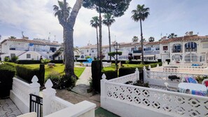 A courtyard with white buildings, palm trees, and a white fence. - Lago Jardin Costa Blanca  (Torrevieja)