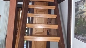 Un escalier en bois, doté d’une structure sombre, mène à une pièce dont un mur est blanc et qui contient un tableau encadré.