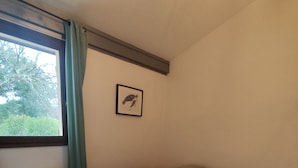 Un dormitorio con cama, un radiador, una ventana con cortinas y un cuadro enmarcado en la pared.