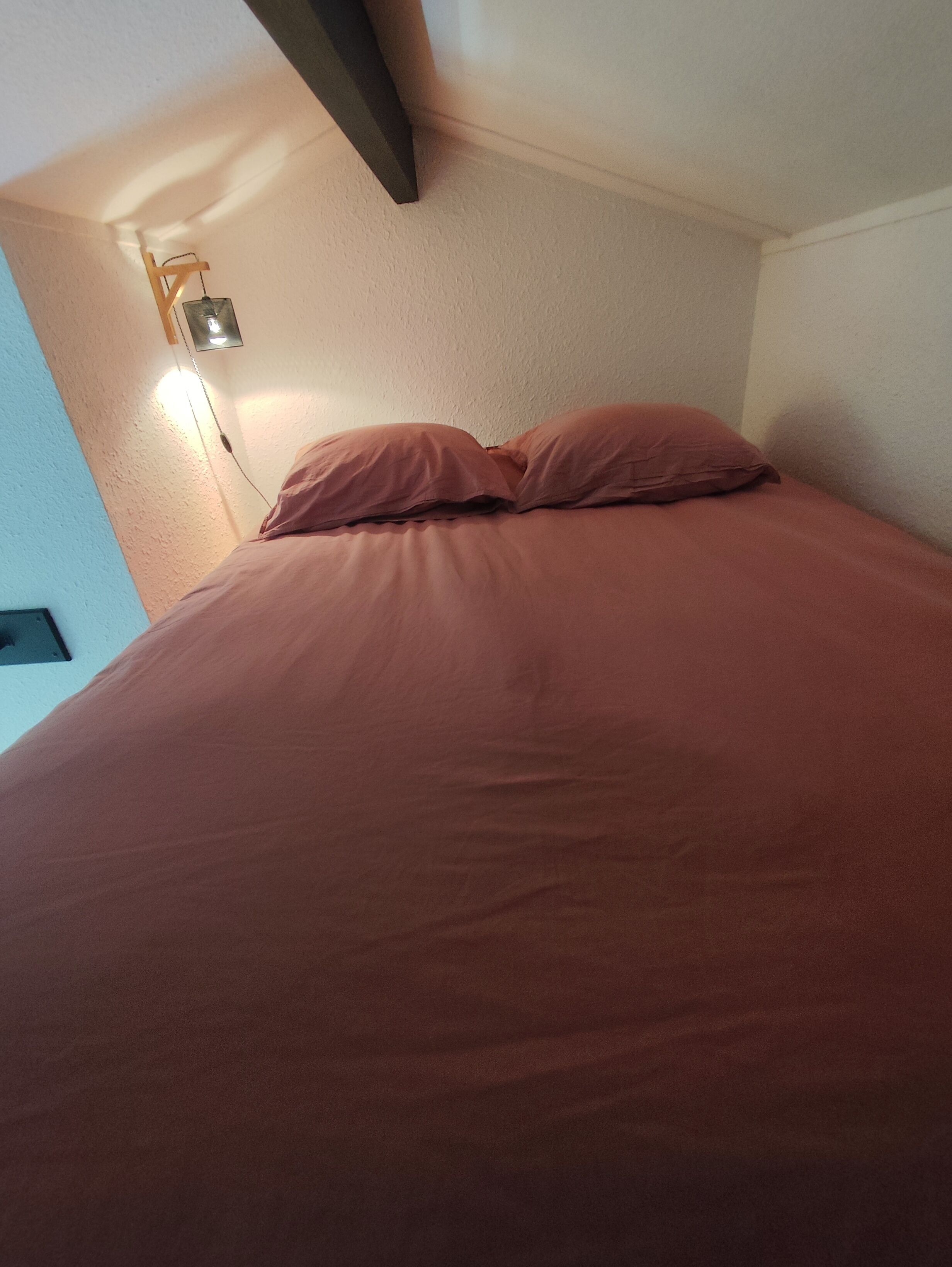 A bed with a headboard, a wall-mounted light, and a textured wall.