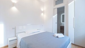 A modern bedroom with a bed, nightstand, wardrobe, and built-in lighting.