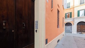 A narrow street with a building featuring a large wooden door and a beige wall.