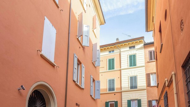 A narrow street with buildings featuring arched doorways and multiple windows with shutters.