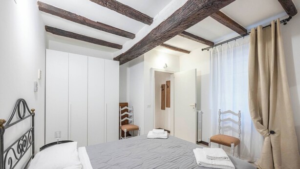 Een slaapkamer met een bed, een stoel, een kledingkast, en een zichtbare badkamer door een geopende deur.