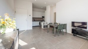 Een moderne woonkamer met een eethoek, een keuken op de achtergrond en een flatscreen aan de muur.
