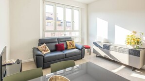 Een moderne woonkamer met een zwarte leren bank, een eettafel en een keuken met een marmeren aanrecht.