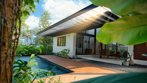 Ett modernt hus med en swimmingpool, omgivet av frodig grönska.