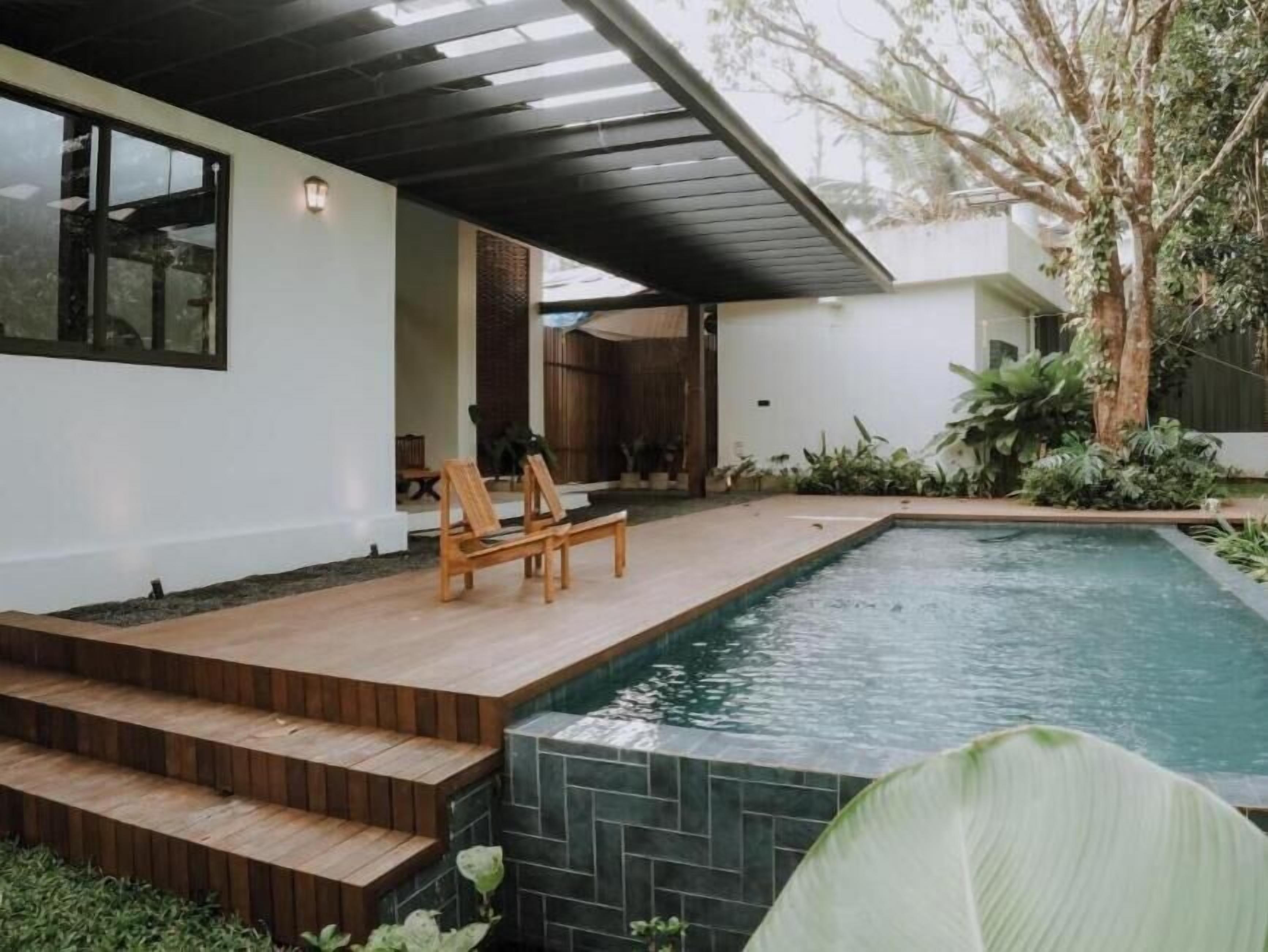 A modern outdoor pool area with wooden steps leading to a seating area, surrounded by greenery.