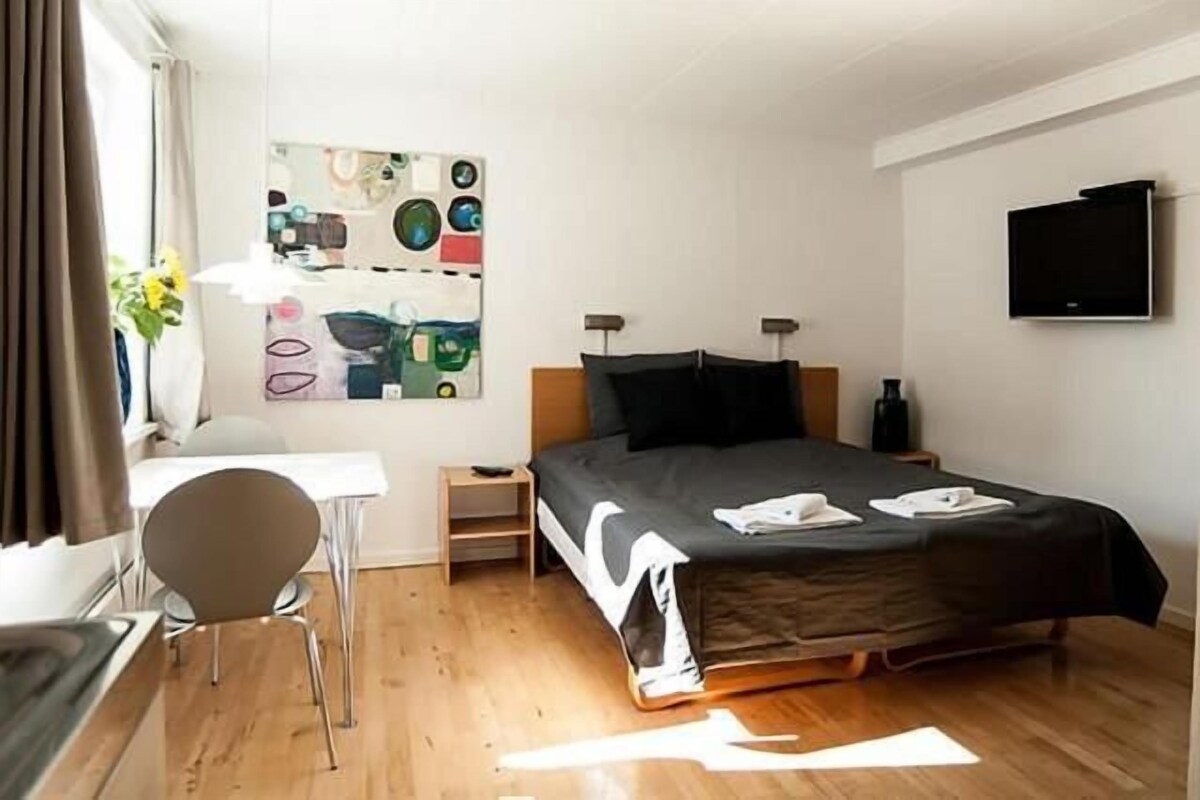 Een hotelkamer met een bed, een bureau, een stoel, een televisie en een kunstwerk aan de muur.