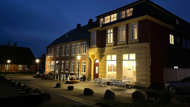A hotel with a traditional facade, outdoor seating, and a well-lit entrance. - Marsk Hotellet (Højer)