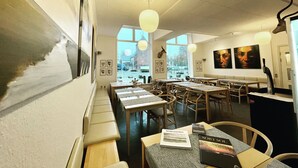 A restaurant interior with tables, chairs, artwork on the walls, and a view through the windows. - Marsk Hotellet (Højer)
