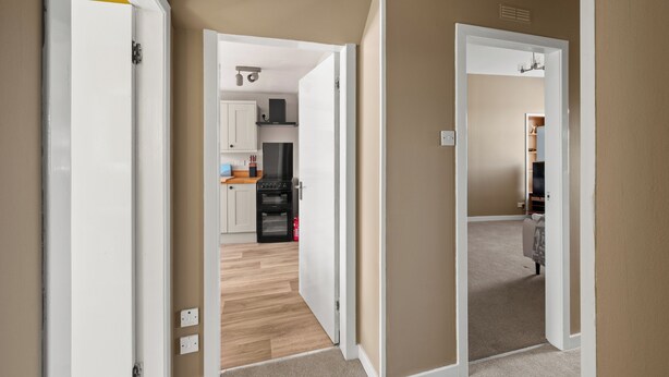 Ein Flur, der zu einer Küche mit Holzboden, weißen Schränken und einem schwarzen Kühlschrank führt.