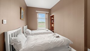 Ein Schlafzimmer mit zwei Betten, einem Fenster mit Jalousien, einem Bücherregal und einer Deckenleuchte.