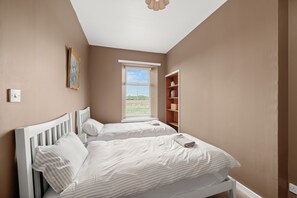A bedroom with two beds, a window with blinds, a bookshelf, and a ceiling light fixture. - Home in Perth and Kinross (Coupar Angus)