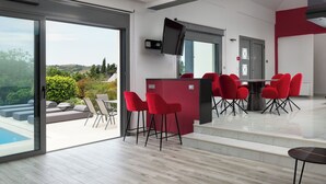 A modern interior with a pool view, a bar area, and red chairs. - Rosa D'oro (Maritsa)