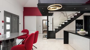 A modern kitchen with a marble island, red chairs, and a black staircase. - Rosa D'oro (Maritsa)