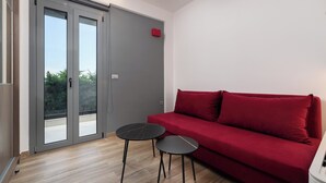 A room with a red sofa, two small tables, a sliding glass door, and a white wall. - Rosa D'oro (Maritsa)