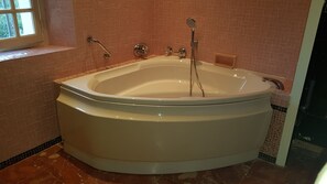 Una vasca da bagno indipendente e spaziosa in un bagno con pareti piastrellate in rosa e una finestra.