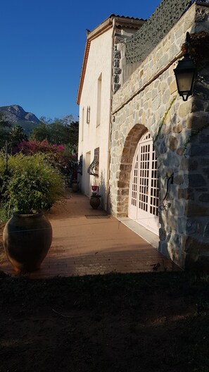A stone building with a tiled roof, a large potted plant, and a pathway leading to an arched entrance. - GRAPI Farm with a swim spa for 4 adults and 4 children (CALVI)
