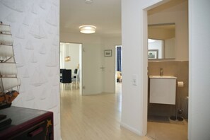 A modern interior with a dining area, a hallway leading to a bathroom, and a visible door. - Tannenburg Apartment 107 - A Beachfront Vacation with Room for the Whole Family (Grömitz)