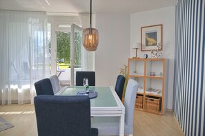 A dining area with a glass table, chairs, a hanging light fixture, and a bookshelf with decorative items. - Tannenburg Apartment 107 - A Beachfront Vacation with Room for the Whole Family (Grömitz)