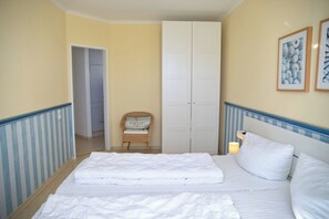 A hotel room with a bed, a wardrobe, a chair, and framed artwork on the wall. - Tannenburg Apartment 107 - A Beachfront Vacation with Room for the Whole Family (Grömitz)