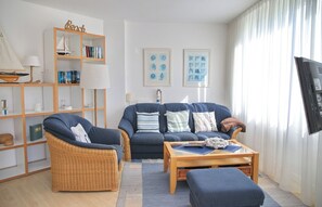 A living room with a sofa, armchair, coffee table, bookshelf, and artwork on the walls. - Tannenburg Apartment 107 - A Beachfront Vacation with Room for the Whole Family (Grömitz)