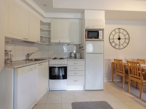 A compact kitchen with white cabinetry, a microwave, a refrigerator, a stove, and a dining area with wooden chairs and a table. - Levistar 912 - 2BR Apt with Sauna (Kittilä)