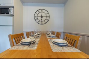 A dining room with a wooden table set for six, a wall clock, and a microwave above the refrigerator. - Levistar 912 - 2BR Apt with Sauna (Kittilä)