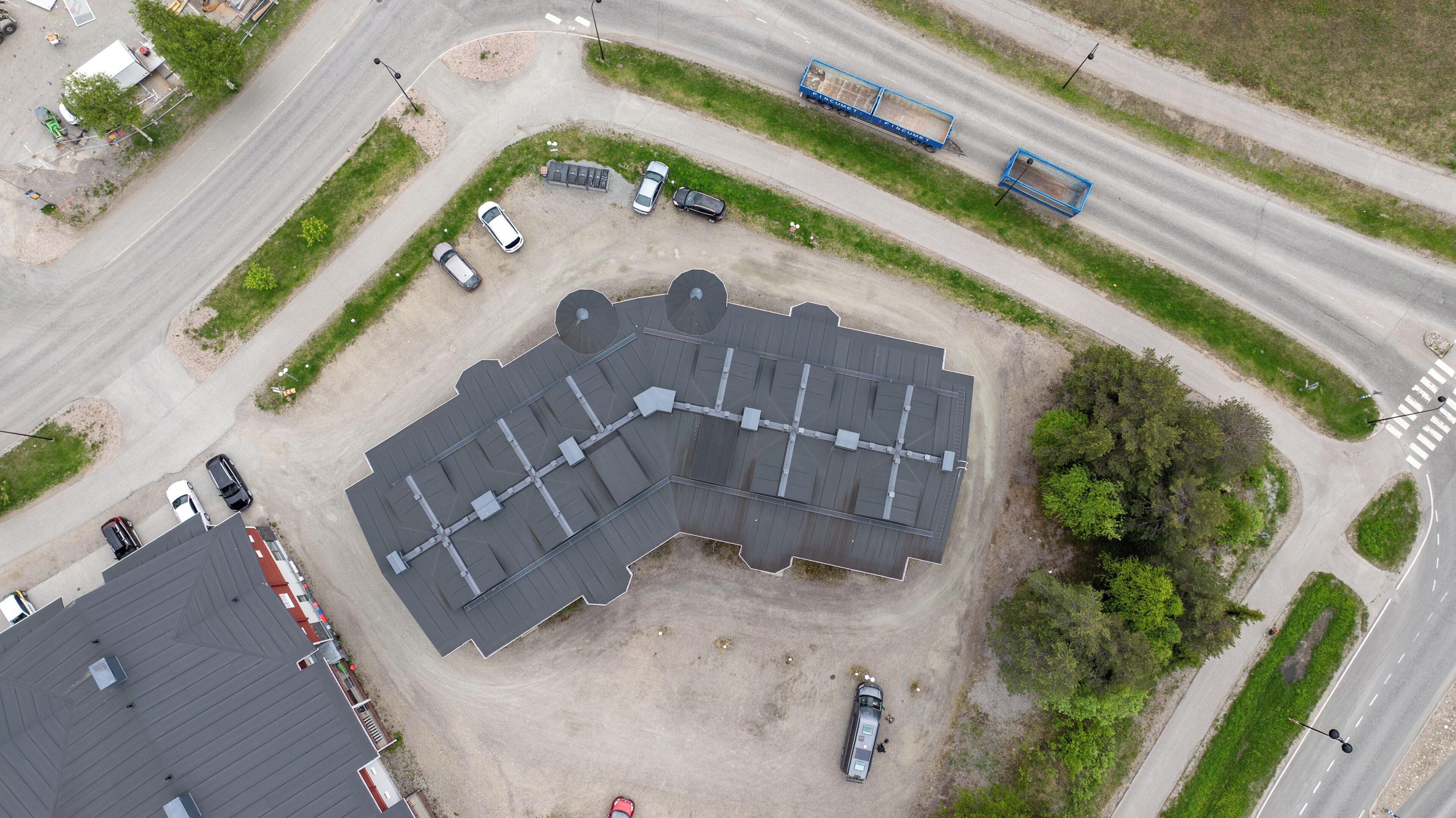 An aerial view of a parking lot with multiple cars and a large building with a grey roof.