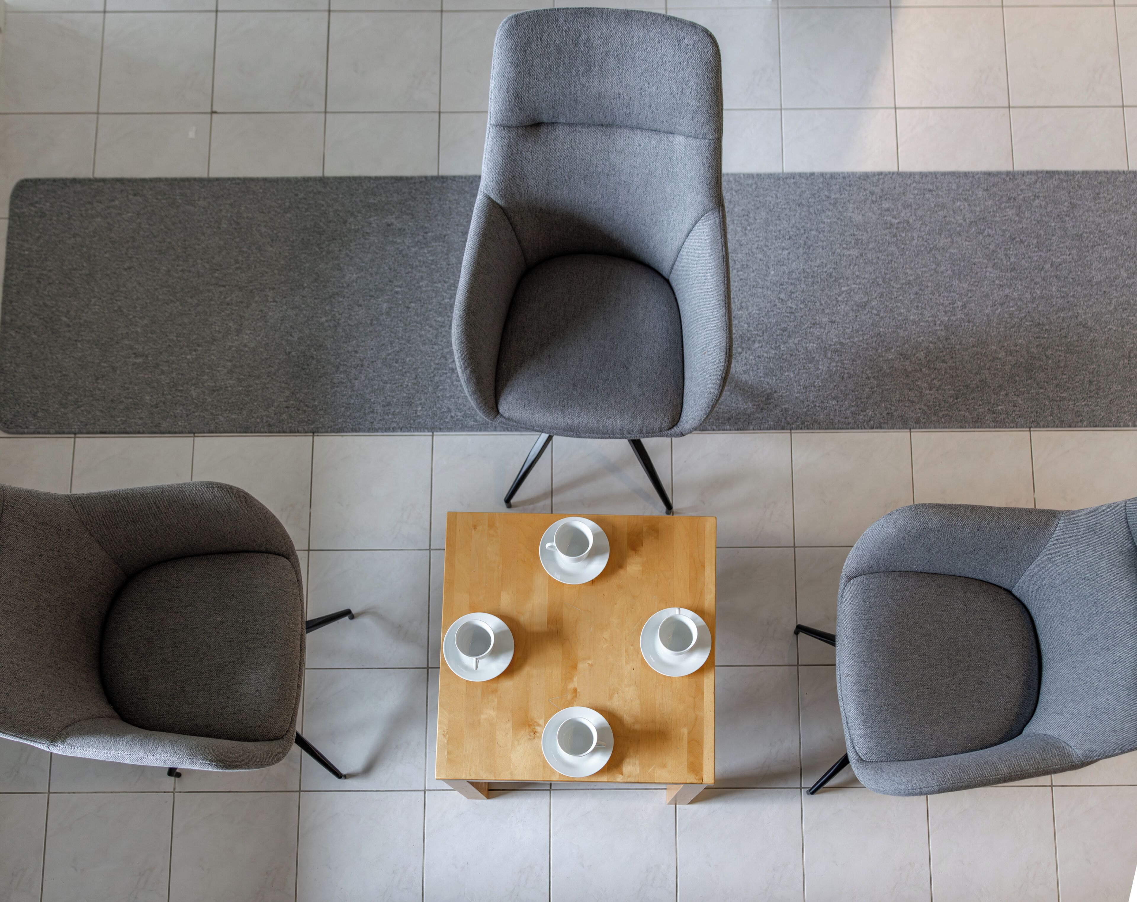 Vue plongeante d’une pièce avec une table en bois, quatre fauteuils gris et un tapis gris.