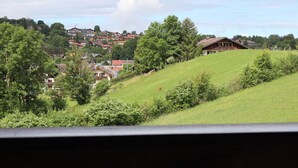 A rural landscape with houses on a hillside, a wooden building with a sloped roof, and a cow grazing. - Berghof Vacation Rentals, Dorfblick Apartment, Zugspitz Region (Bad Kohlgrub)