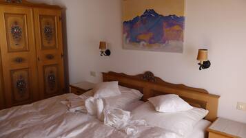 Ein ordentlich bezogenes Bett mit weißen Leinen, ein hölzerner Kopfseitenverkleidung, ein Nachttisch mit Lampe und ein Bergpanorama an der Wand.