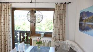 A dining area with a table, chairs, a vase with flowers, a hanging light fixture, and a view of greenery outside. - Berghof Vacation Rentals, Dorfblick Apartment, Zugspitz Region (Bad Kohlgrub)