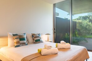 Habitació d'hotel amb llit, almoines, tovellons, una làmpada i una porta corredissa de vidre que dona a una zona exterior.
