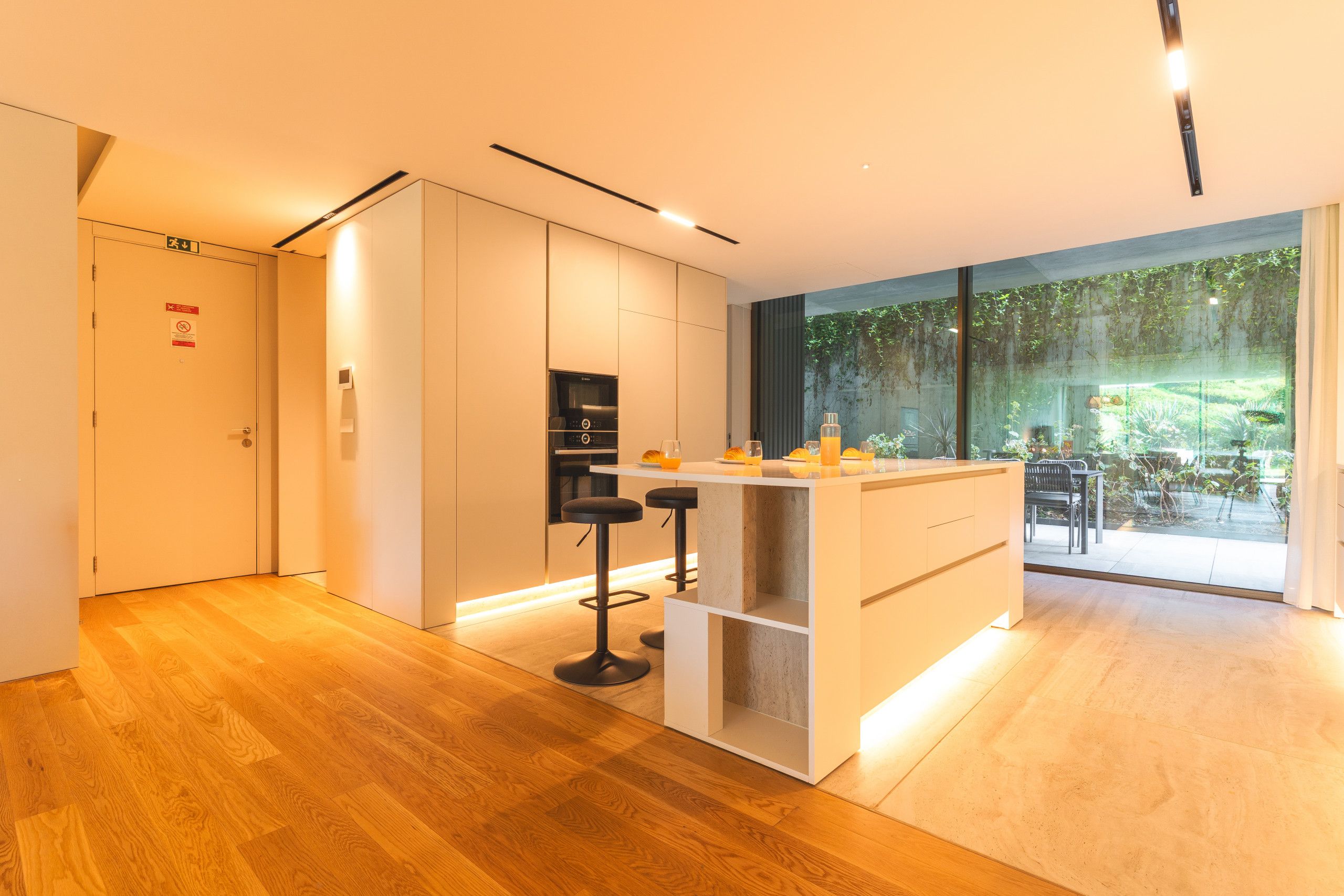 A modern kitchen with a bar area, wooden flooring, and a view of greenery outside.