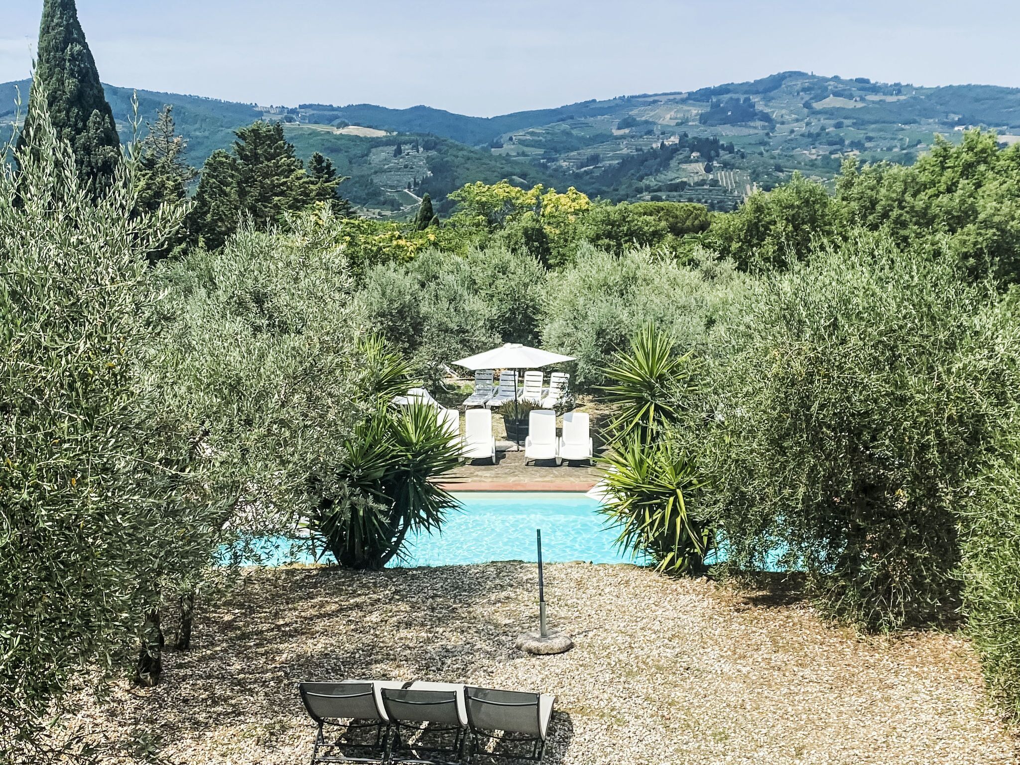 A pool area with lounge chairs and umbrellas, surrounded by dense vegetation and hills in the background.
