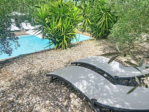 A poolside area with lounge chairs, pebbles, and green foliage. - La Camporena by Interhome (Greve in Chianti)