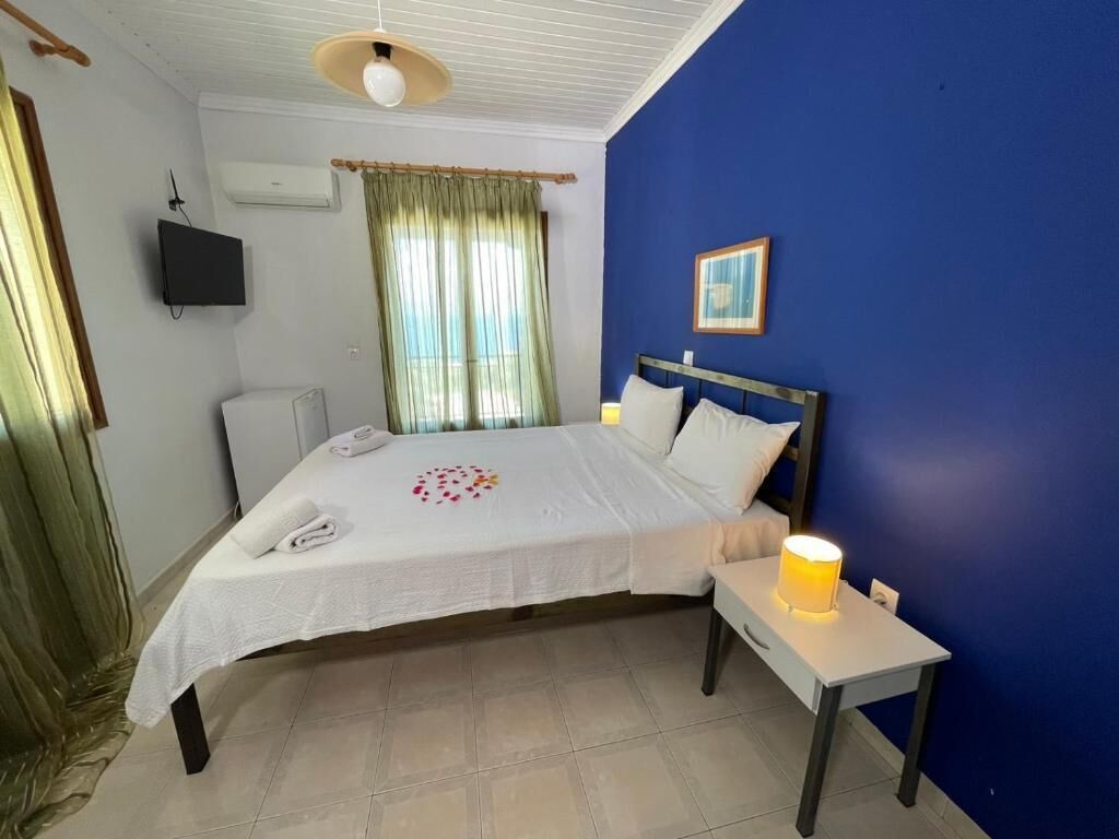 Un dormitorio con cama, mesita de noche, televisor montado en la pared, aire acondicionado y ventana con cortinas.