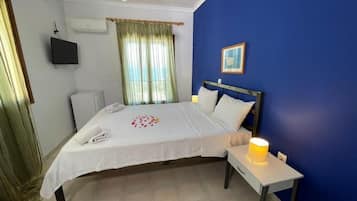 Un dormitorio con cama, mesita de noche, televisor montado en la pared, aire acondicionado y ventana con cortinas.